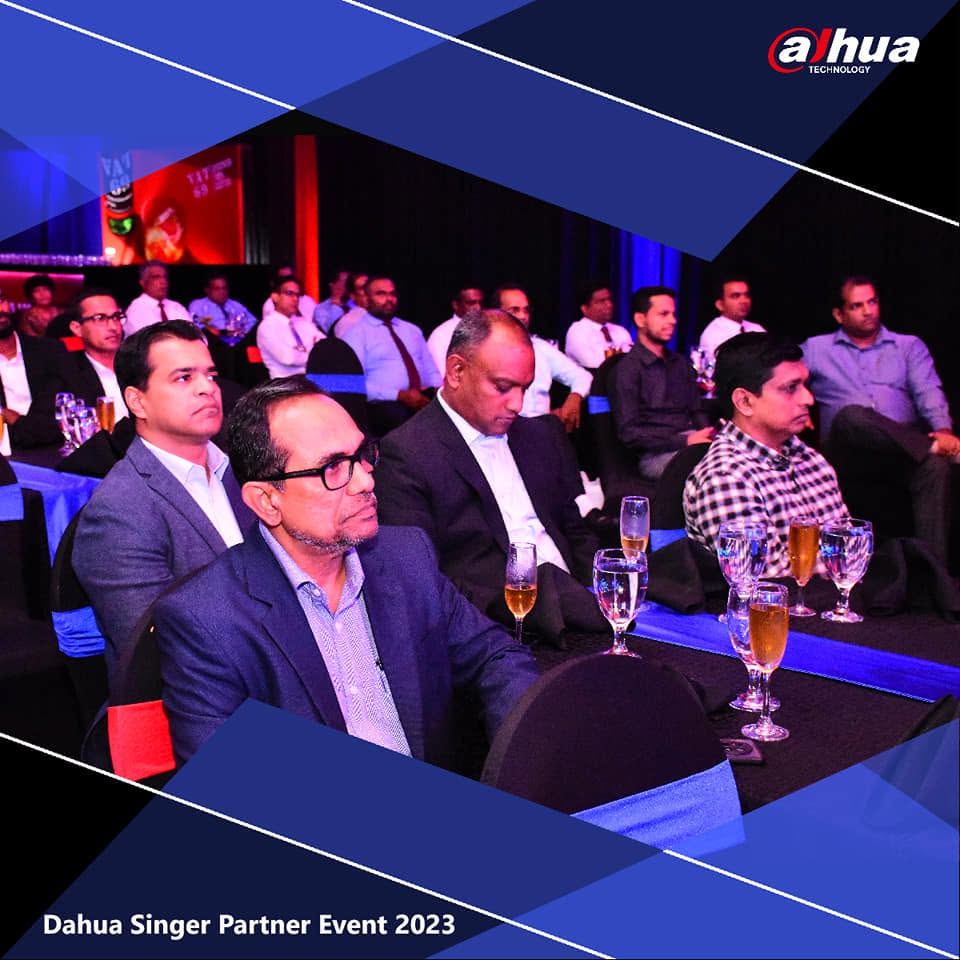 Partners seated at a blue-lit corporate event, watching a presentation